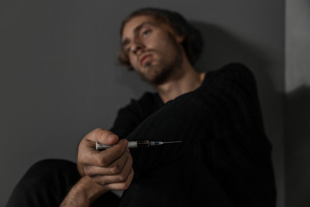 Young drug addict with syringe sitting near gray wallの写真素材