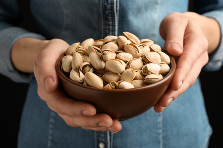 Woman holding bowl with pistachio nuts on black background, closeupの写真素材