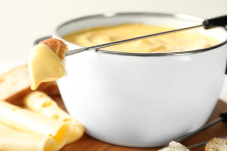 Pot of delicious cheese fondue and fork with bread on tableの写真素材