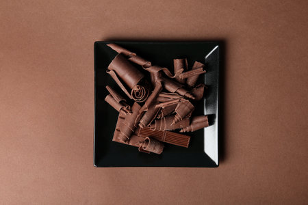 Plate with chocolate curls and pieces on color background, top viewの写真素材
