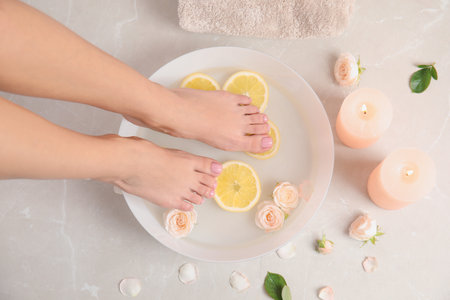 Woman putting her feet into bowl with water, roses and lemon slices on floor, top view. spa treatmentの写真素材