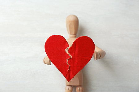 Wooden puppet with torn cardboard heart on gray background. relationship problemsの写真素材