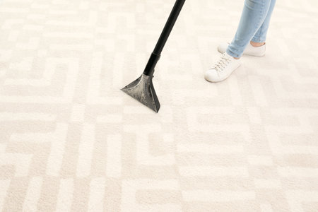 Woman removing dirt from carpet with vacuum cleaner indoors, closeup. Space for textの写真素材