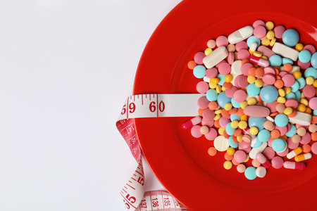 Plate with weight loss pills and measuring tape on white background, top view. Space for textの写真素材