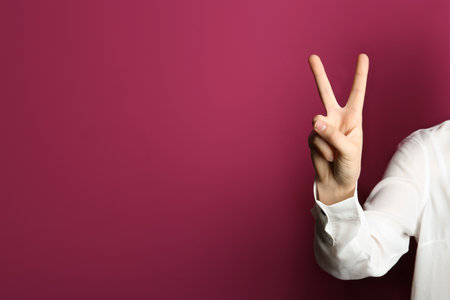 Young woman showing victory gesture on color background. Space for textの写真素材