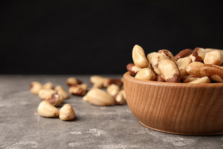 Bowl with tasty Brazil nuts on gray table. Space for text