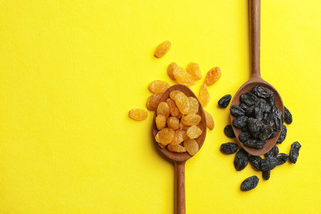 Spoons with raisins and space for text on color background, top view. Dried fruit as a healthy snackの写真素材