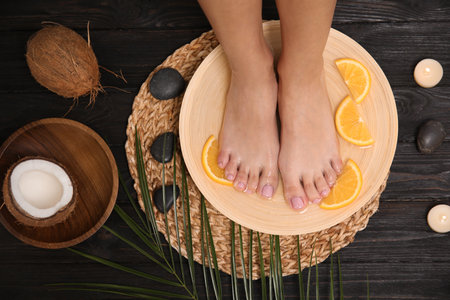 Woman soaking her feet in plate with water and orange slices on wooden floor, top view. spa treatmentの写真素材