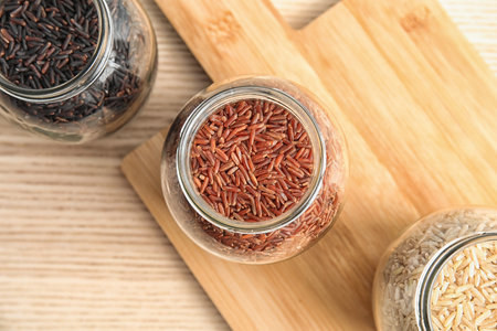 Jars with different types of rice and board on wooden table, top viewの写真素材