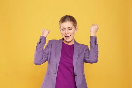Happy young businesswoman celebrating victory on color background