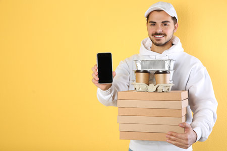 Young man holding orders and smartphone on color background, mockup for design. Online food deliveryの写真素材