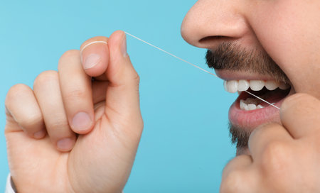 Young man flossing teeth on color background, closeupの写真素材