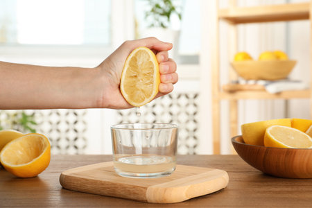 Woman squeezing lemon juice into glass bowl at tableの写真素材