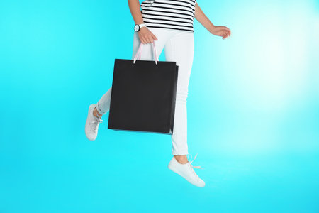 Woman jumping with paper shopping bag on color background. Mock up design