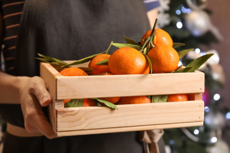 Woman with wooden crate of ripe tangerines and Christmas tree on background, closeupの写真素材