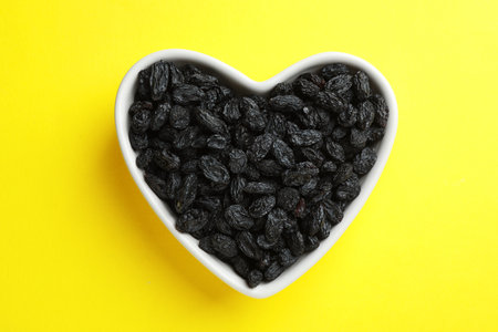 Heart shaped plate with raisins on color background, top view. Dried fruit as a healthy snackの写真素材