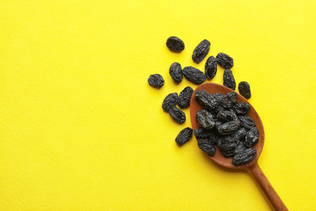 Spoon with raisins and space for text on color background, top view. Dried fruit as a healthy snackの写真素材