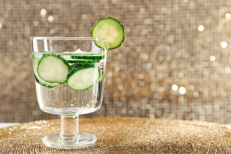 Glass of fresh cucumber water on golden mat. Space for textの写真素材