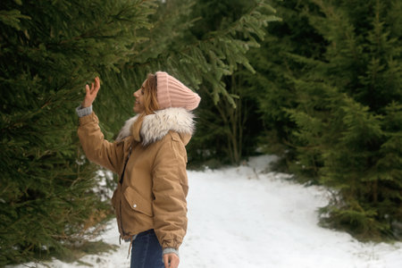 Young woman touching fir branch in snowy forest, space for text. winter holidaysの写真素材