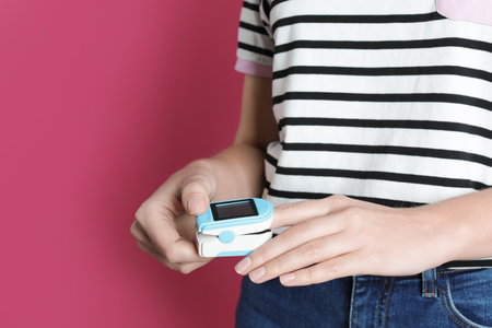 Young woman checking pulse with digital medical device on color background, closeup. Space for text