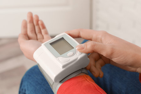 Young woman checking pulse with digital medical device indoors, closeup