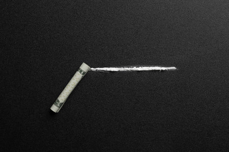 Line of cocaine and rolled money bill on dark background, top viewの写真素材