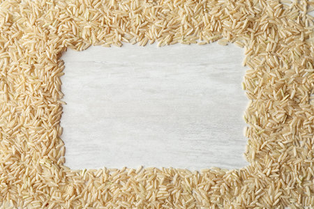 Frame made with brown rice on white wooden background, top view. Space for textの写真素材