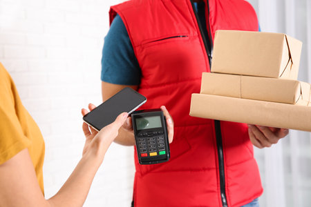 Young woman with smartphone using terminal for delivery payment indoors, closeup