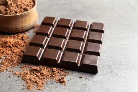 Chocolate bar and cocoa powder on gray background
