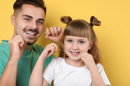 Little girl and her father flossing teeth on color backgroundの写真素材