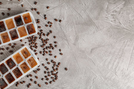 Flat lay composition with ice cubes in trays and coffee beans on gray background. Space for textの写真素材