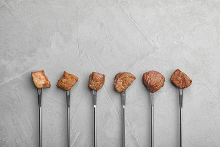 Forks with fried meat fondue pieces on gray background, top view. Space for textの写真素材
