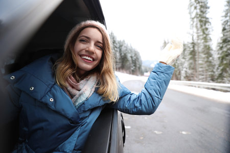 Young woman driving car and looking out of window on road. winter holidays