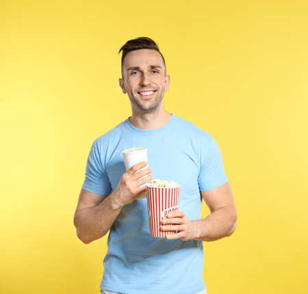 Man with popcorn and beverage during cinema show on color backgroundの写真素材