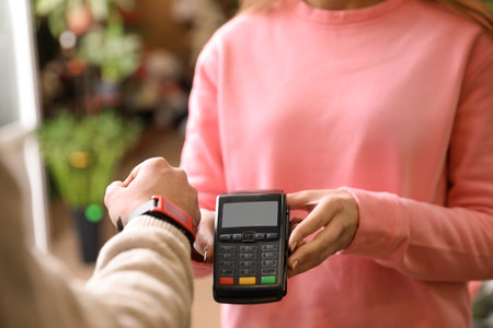Customer using terminal for contactless payment with smartwatch in floral shop, closeupの写真素材