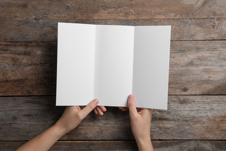 Woman with blank brochure on wooden background, above view. Mock up design