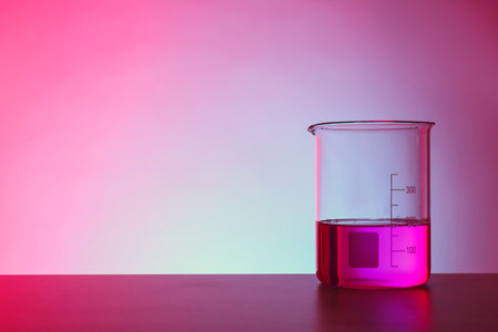 Beaker with liquid on table against color background. Chemistry laboratory glasswareの写真素材