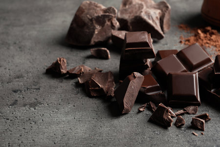 Pieces of chocolate and cocoa powder on gray background