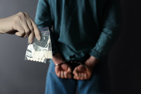 Police worker holding drugs in plastic bags near arrested dealer on color backgroundの写真素材