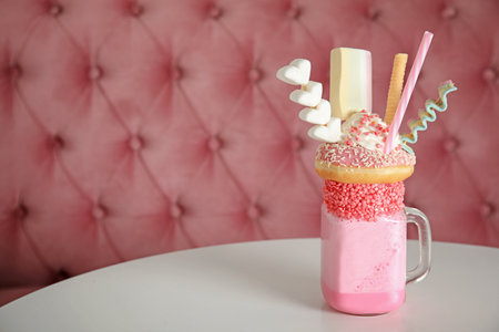 Tasty milk shake with sweets in mason jar on table at cafe. Space for text