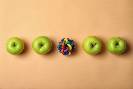 Row of apples with toy ball on color background. be different