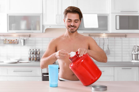 Young shirtless man preparing protein shake at table in kitchenの写真素材