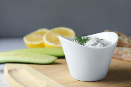 Ceramic bowl of cucumber sauce with ingredients on wooden board, space for text. Traditional...