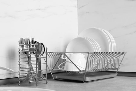 Drying rack with clean dishes near cutlery holder on table in kitchenの写真素材