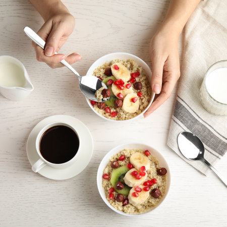 Woman eating quinoa porridge with hazelnuts, kiwi, banana and pomegranate seeds at wooden table, top viewの写真素材