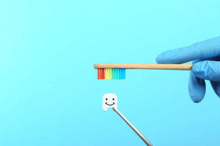 Dentist holding wooden brush near small plastic tooth on color background. Space for textの写真素材