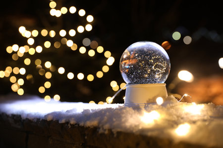 Snow globe and blurred Christmas lights on background. Space for text