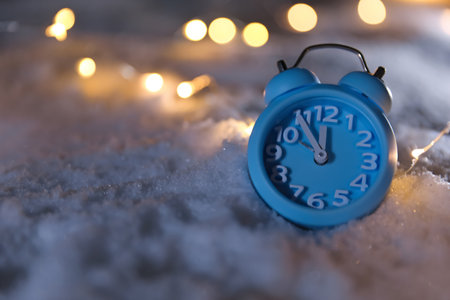 Alarm clock and Christmas lights on white snow outdoors, space for text. midnight count downの写真素材