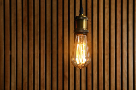 Pendant lamp with light bulb on wooden background. Space for text