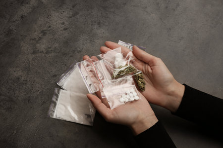 Woman holding plastic bags with cocaine, pills and hemp buds on gray background, closeupの写真素材